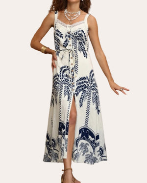 Woman wearing a white dress with blue leaf patterns in an outdoor setting.