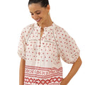 Woman wearing a white blouse with red patterns in a minimalistic setting