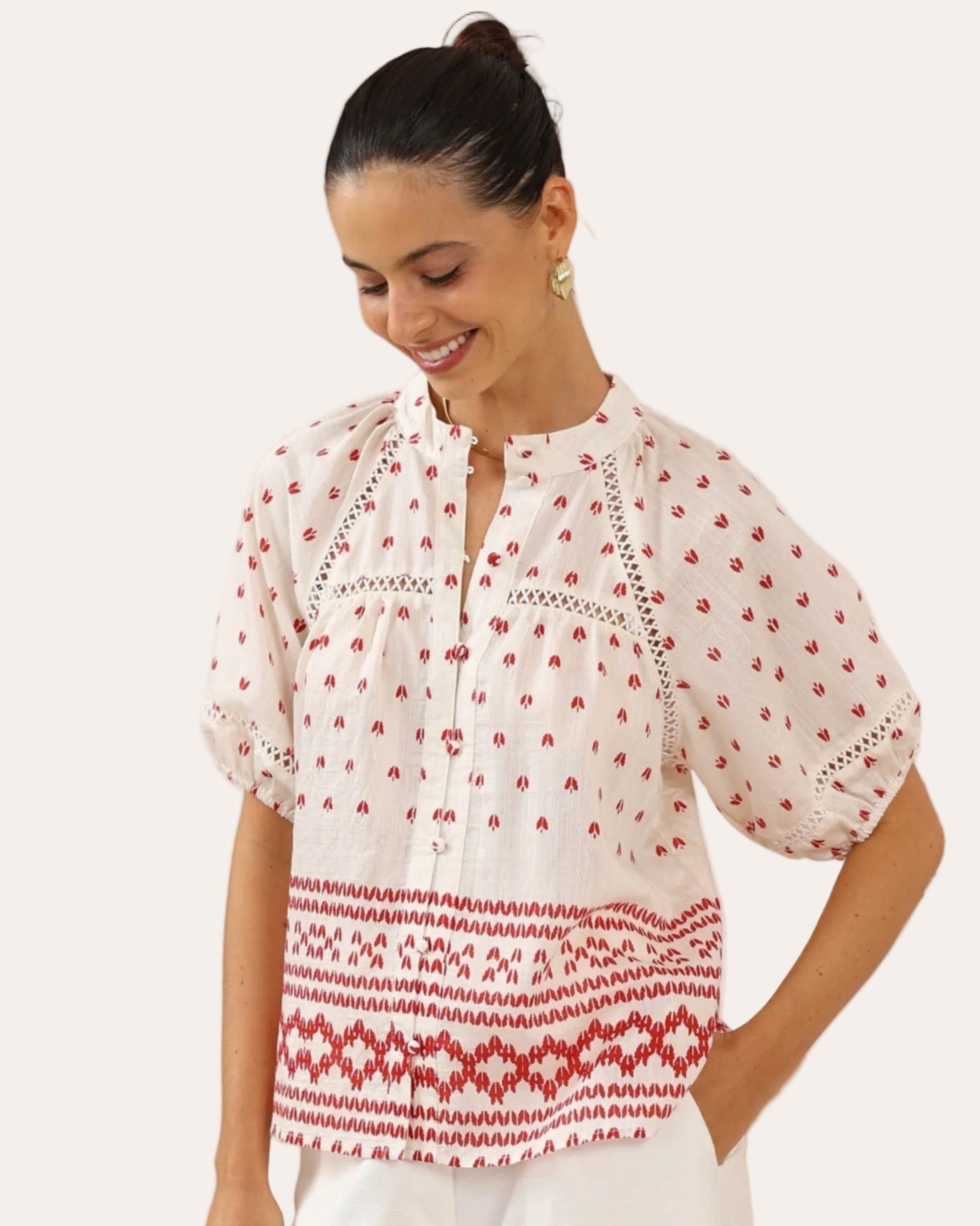 Woman wearing a white blouse with red patterns in a minimalistic setting