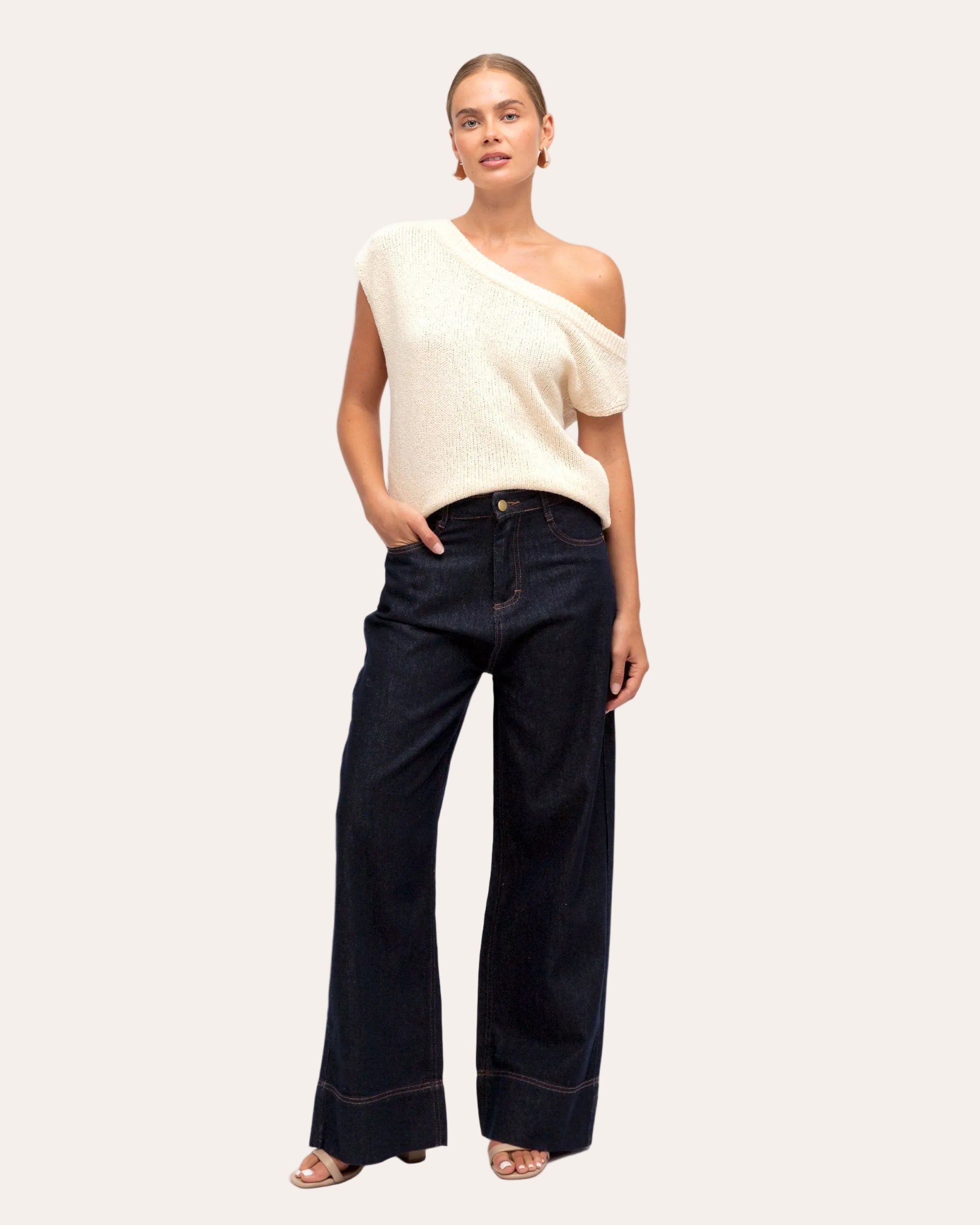 Woman wearing a white sleeveless top and dark blue jeans on a white background