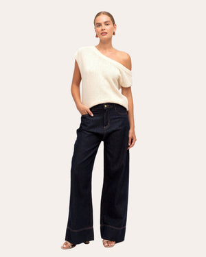 Woman wearing a white sleeveless top and dark blue jeans on a white background