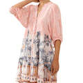 Woman wearing a pink kimono-style garment with a floral pattern in a minimalistic setting.