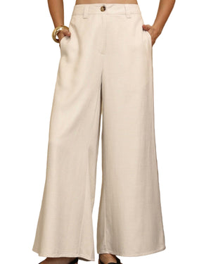 Person wearing white wide-leg pants standing in a room with wooden furniture and decor.