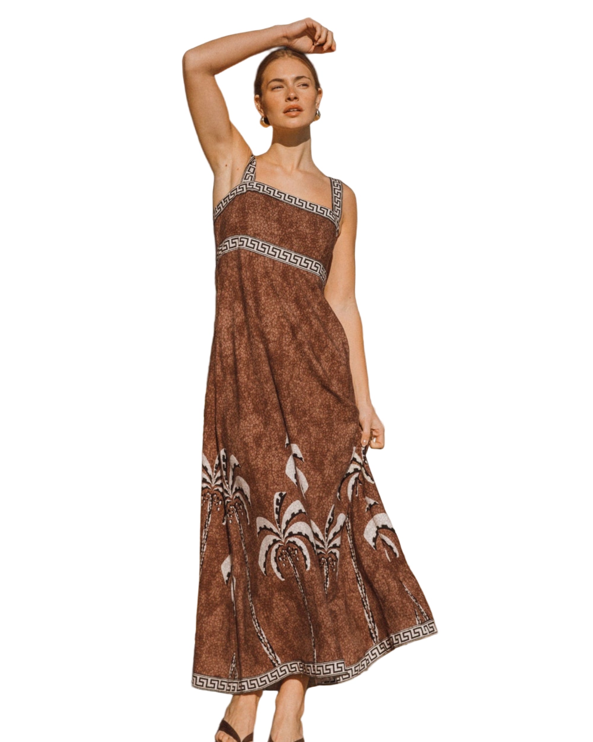 Woman in a brown dress with patterns standing on a sandy path with greenery in the background
